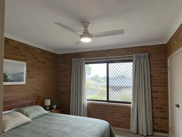 Bedroom with a ceiling fan and light above a bed in a brick-walled home in Morisset