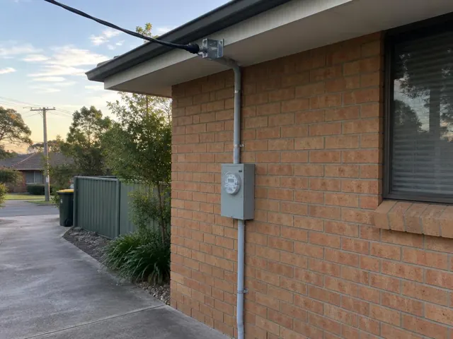 Overhead service cable to a bracket on a brick house wall with meter box and eave in Bonnells Bay